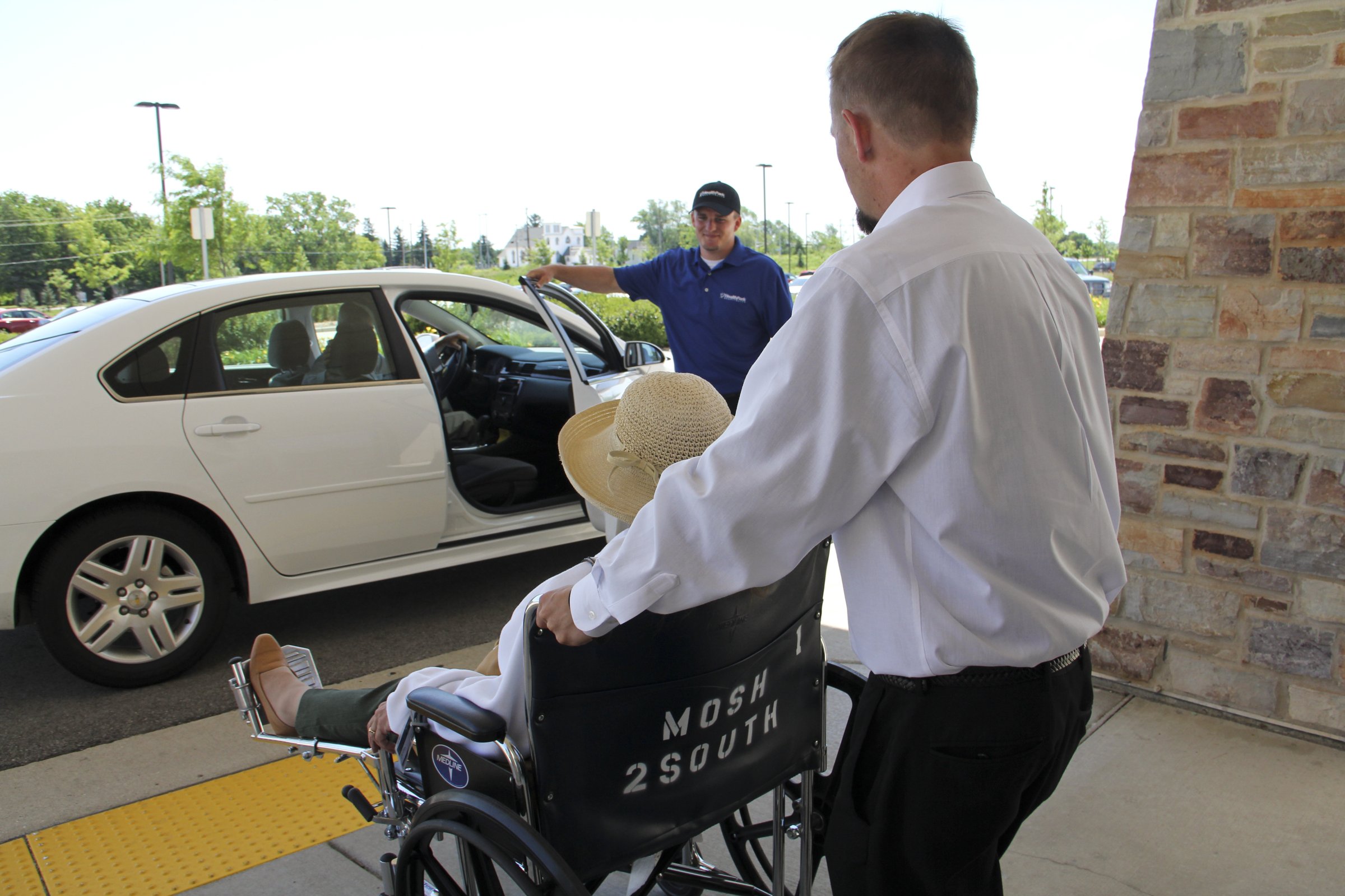 HealthPark attendants assisting a patient in a wheelchair at a clinic entrance